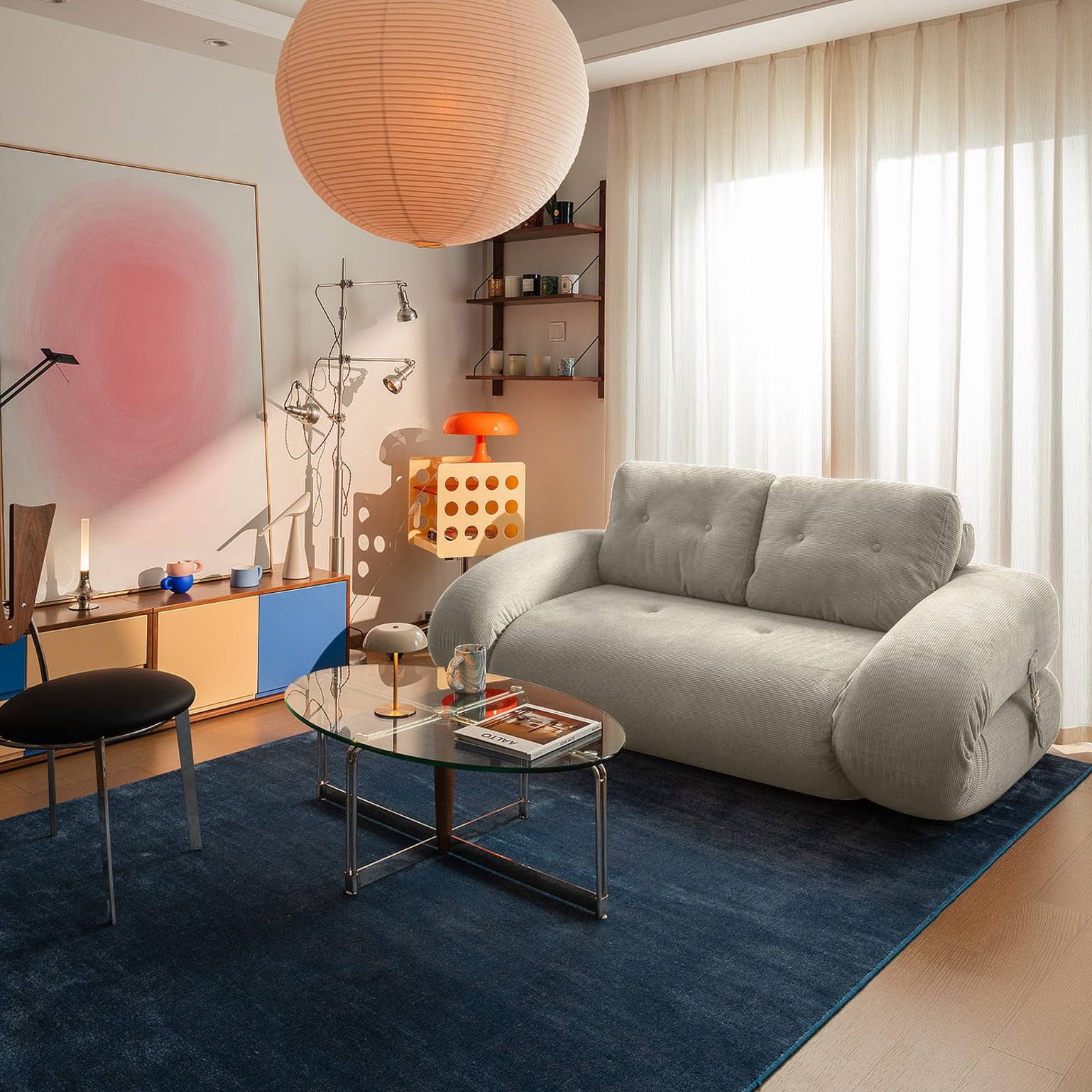 Modern living room with a gray sofa, round pendant light, and blue rug.