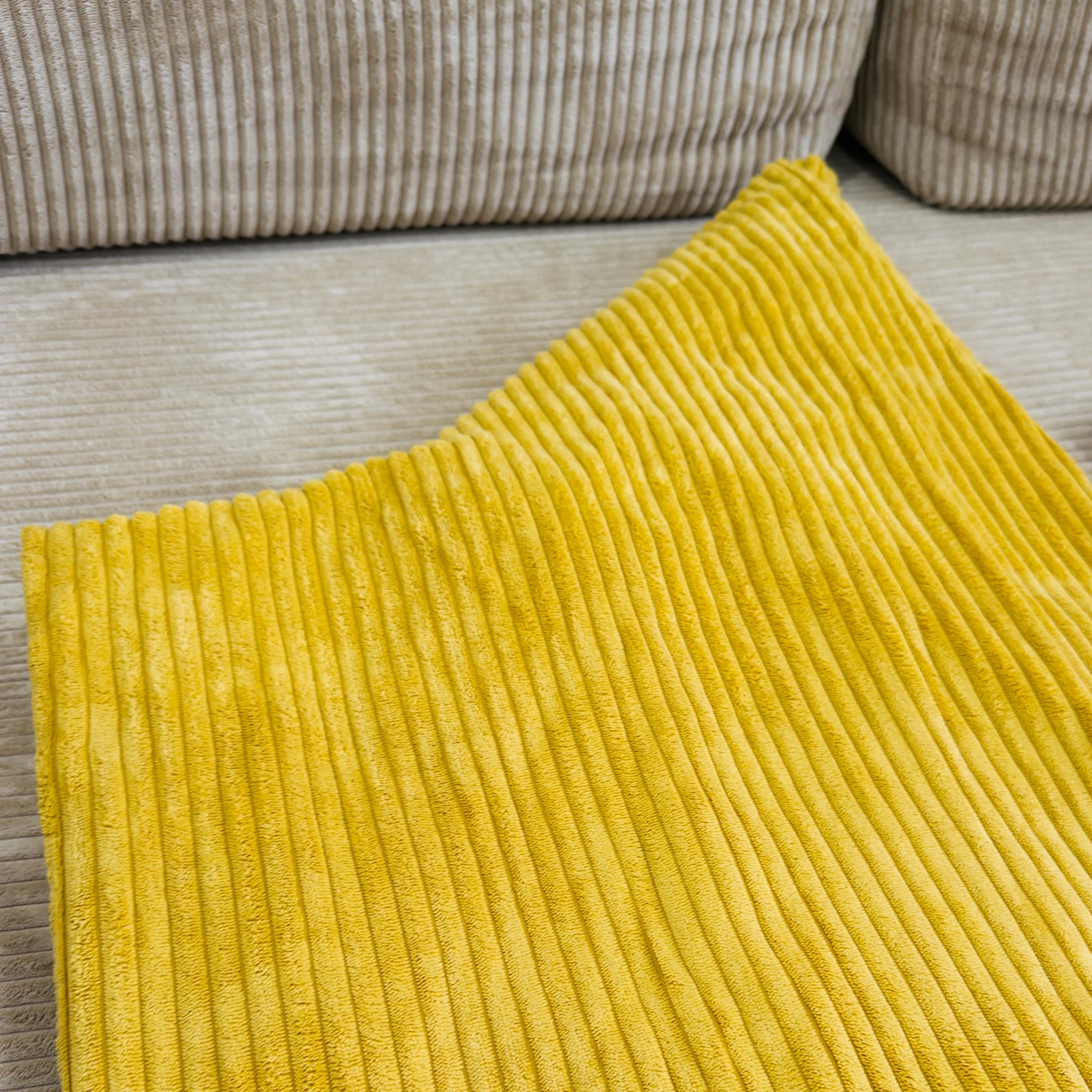 Yellow textured rug on a wooden floor with a beige couch in the background