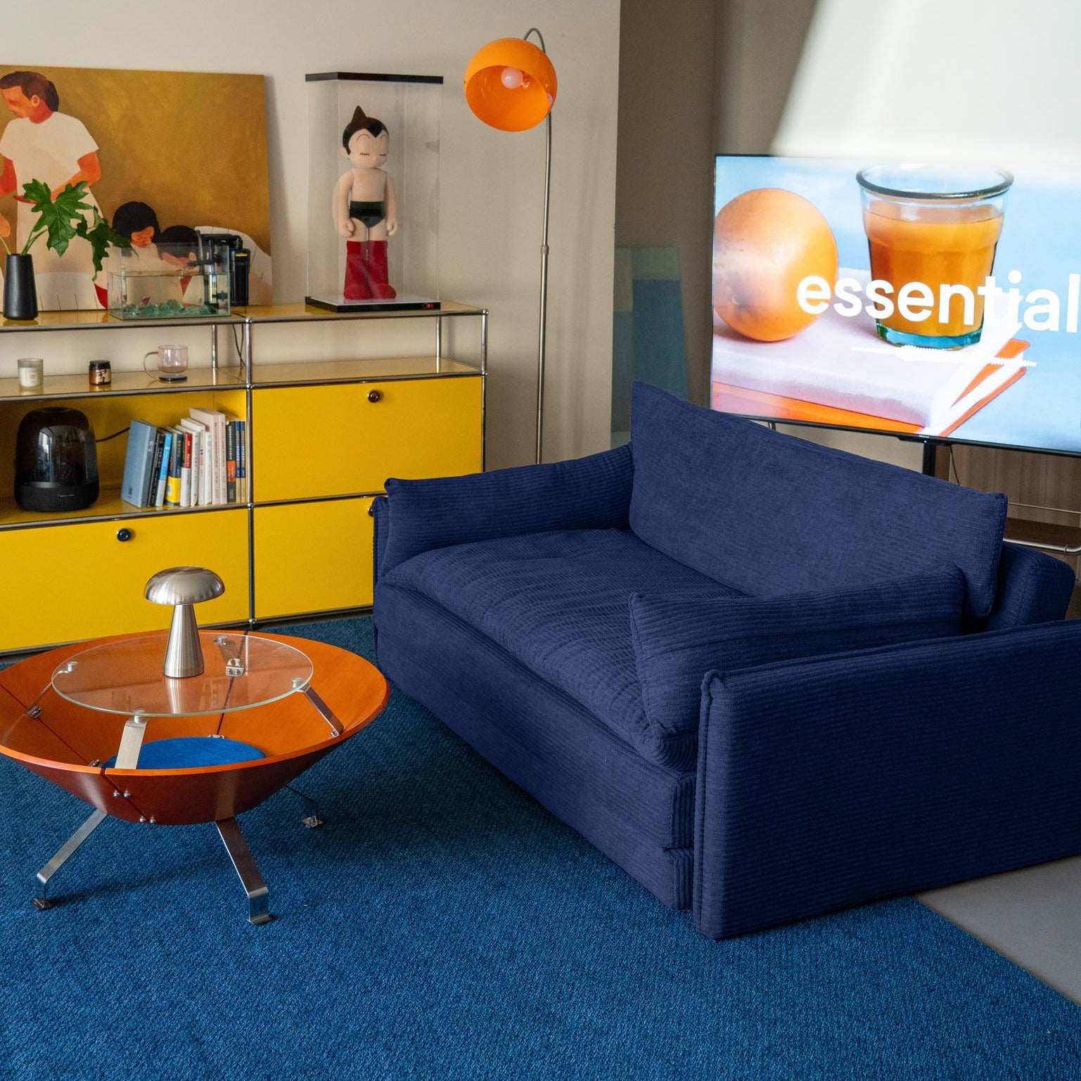 Modern living room with a blue sofa, yellow cabinet, and a TV displaying an advertisement.