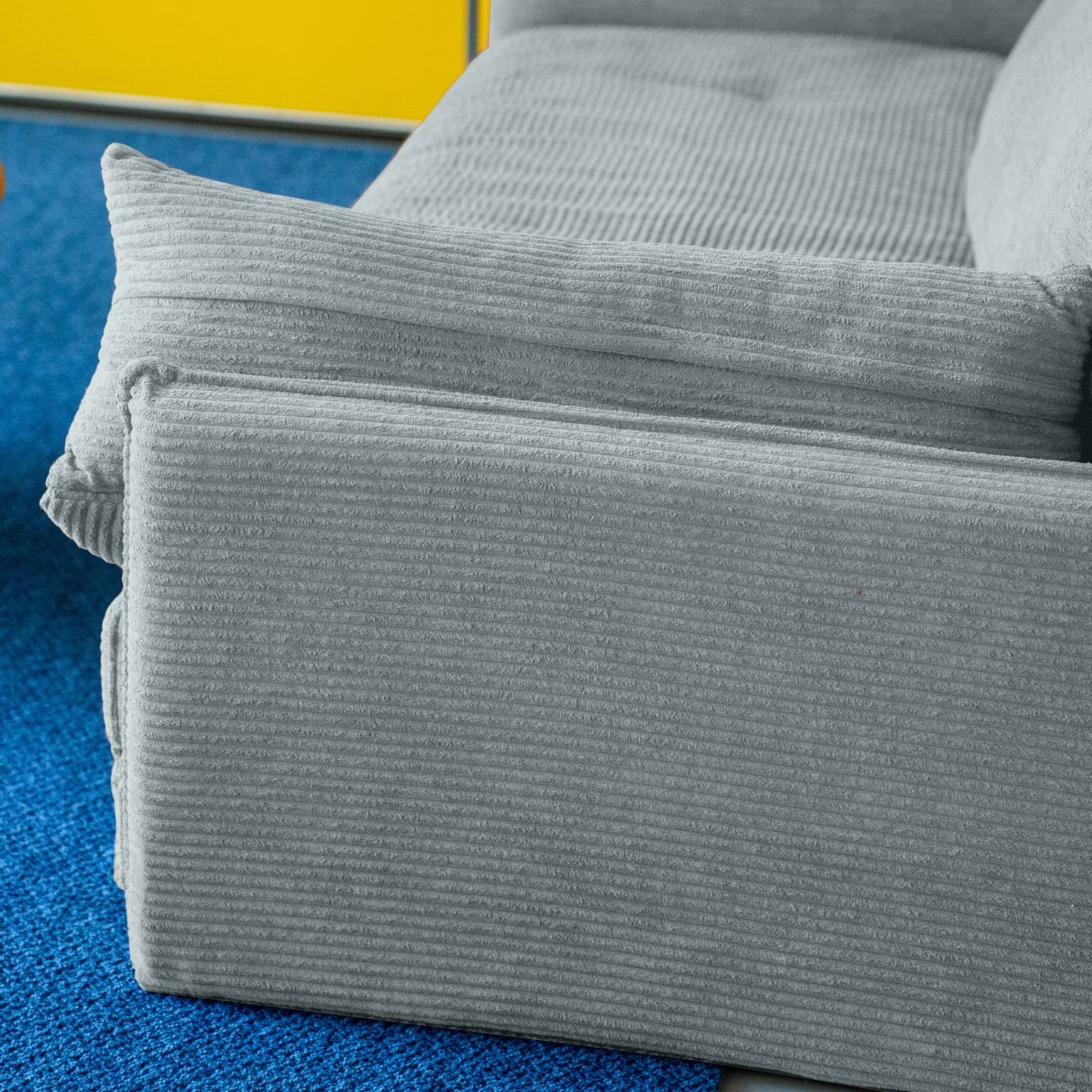 Gray sofa with cushions against a yellow cabinet and blue floor.