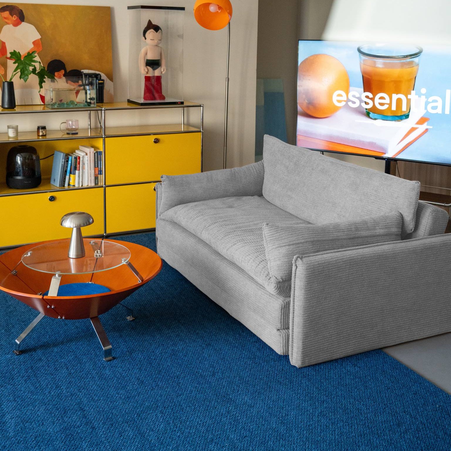 Modern living room with gray sofa, yellow cabinet, and TV displaying a brand logo.