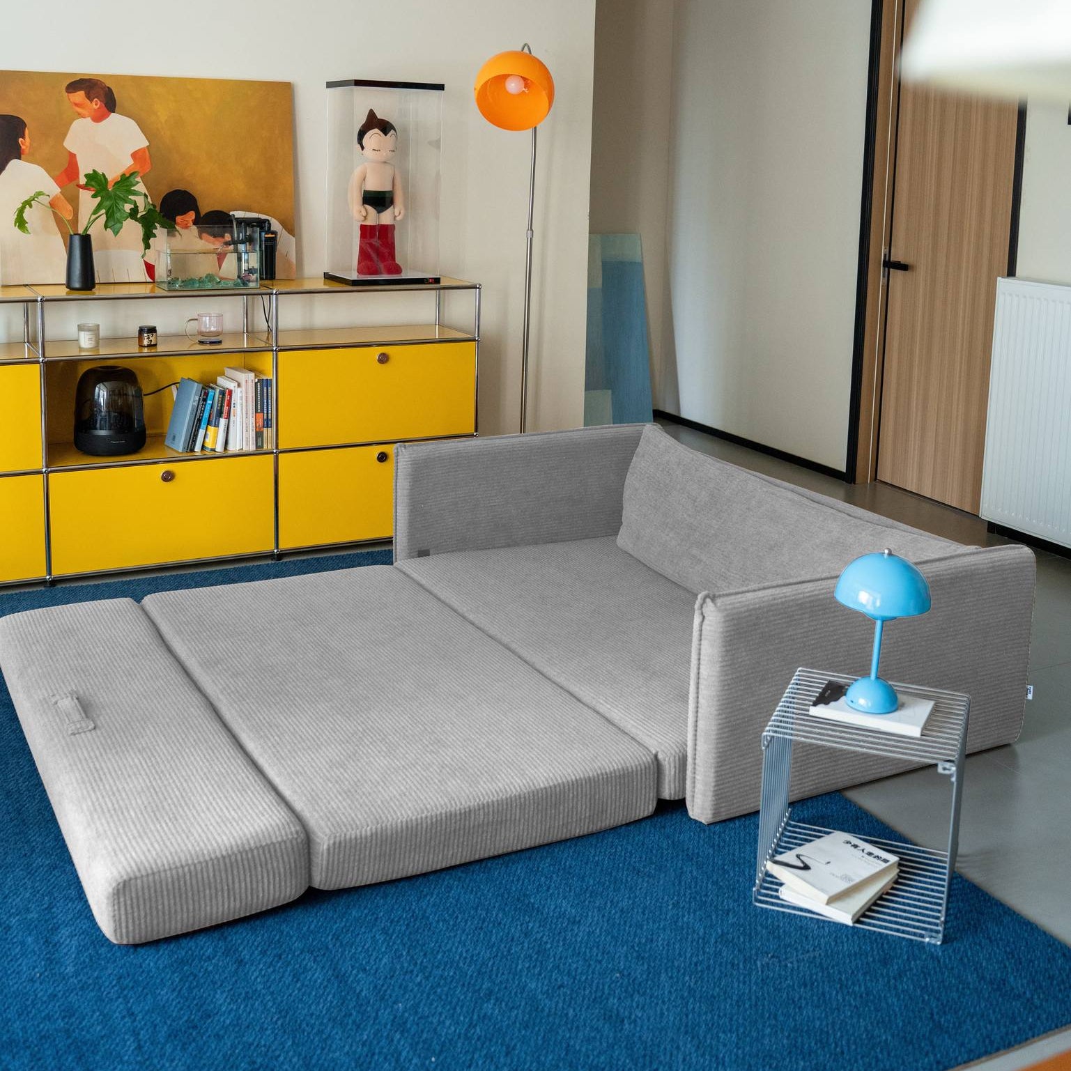 Modern living room with a gray sofa, yellow cabinet, and blue rug.