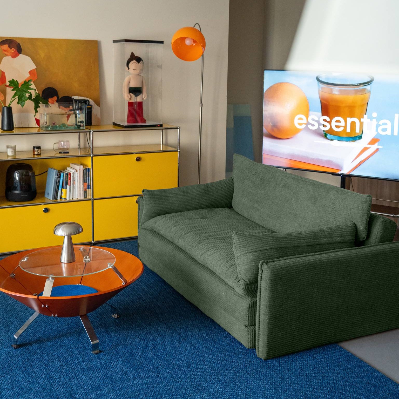 Modern living room with green sofa, yellow cabinet, and TV displaying a juice brand.