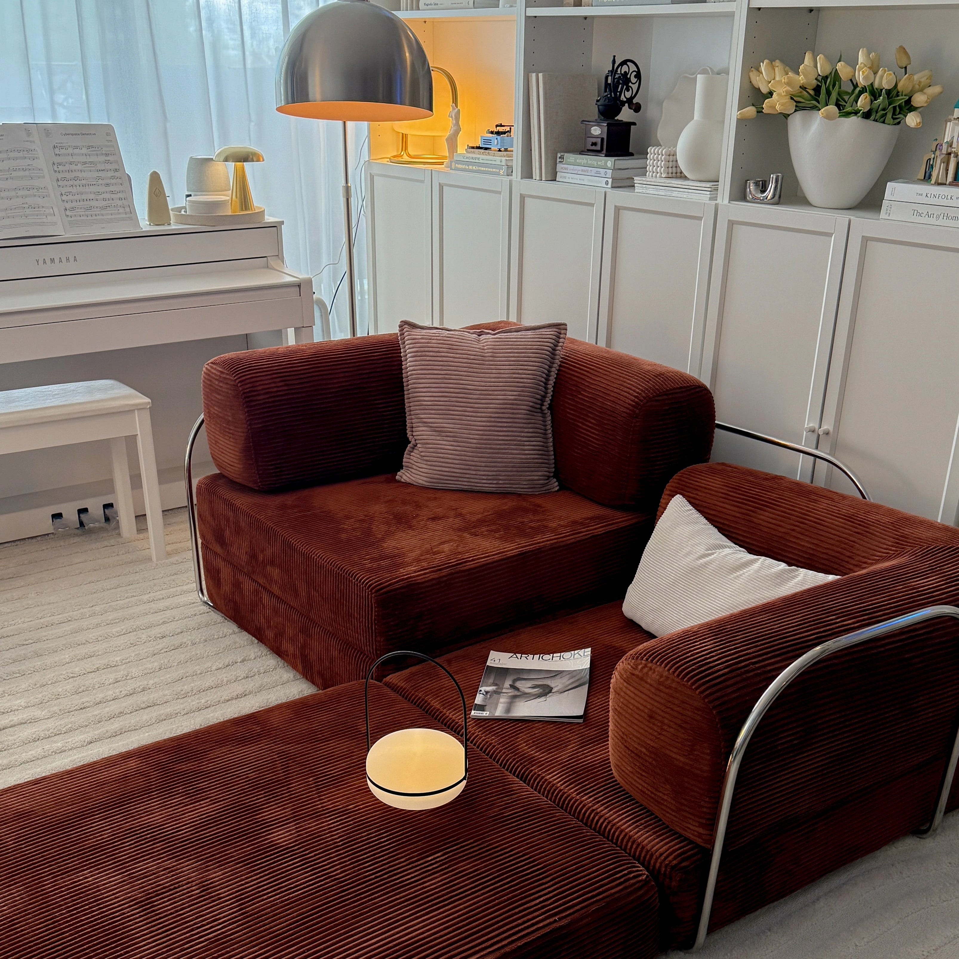 Brown sofa in a living room with a piano and bookshelf in the background.