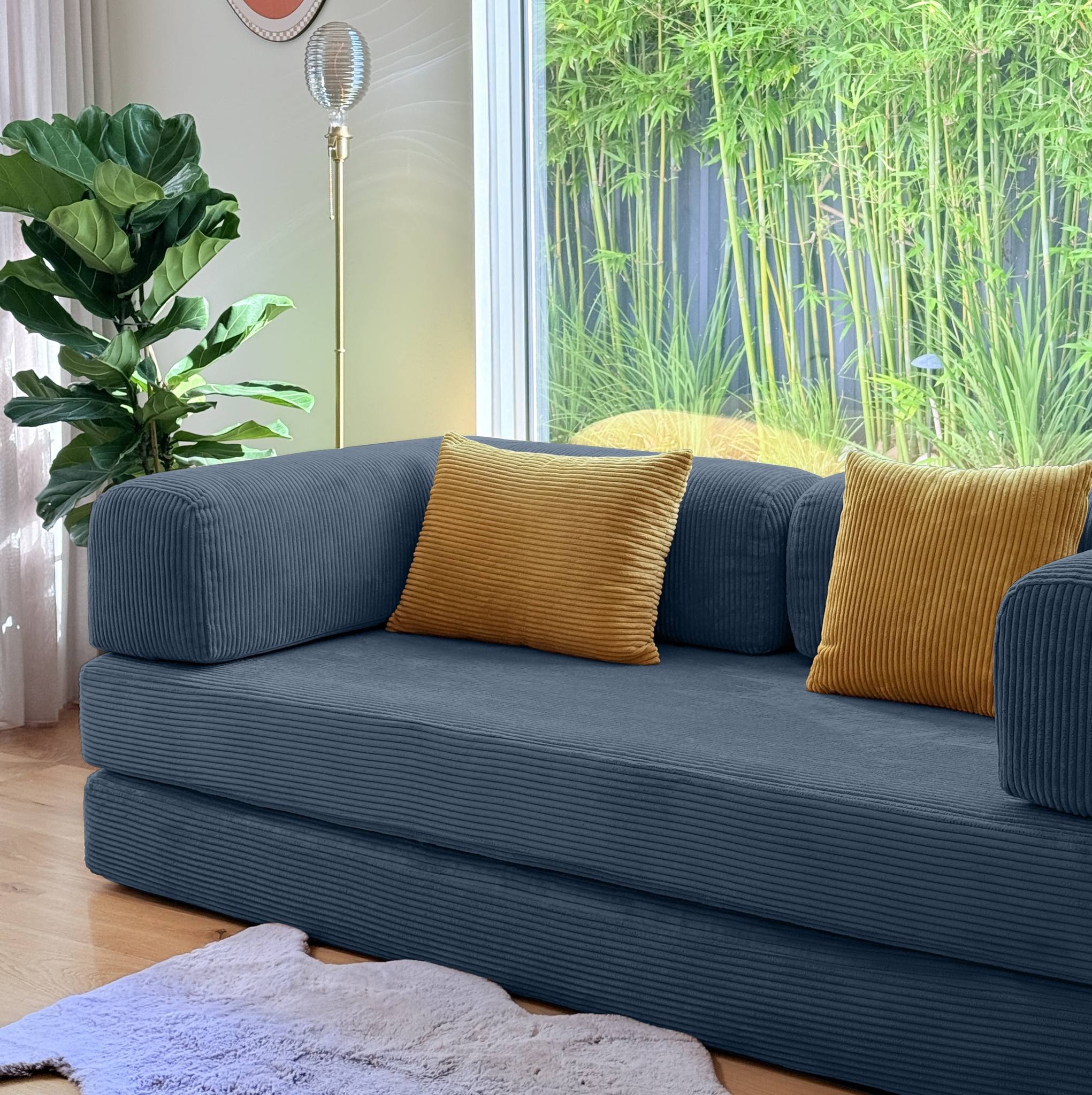 Blue sofa with yellow cushions in a room with a large window and plants.