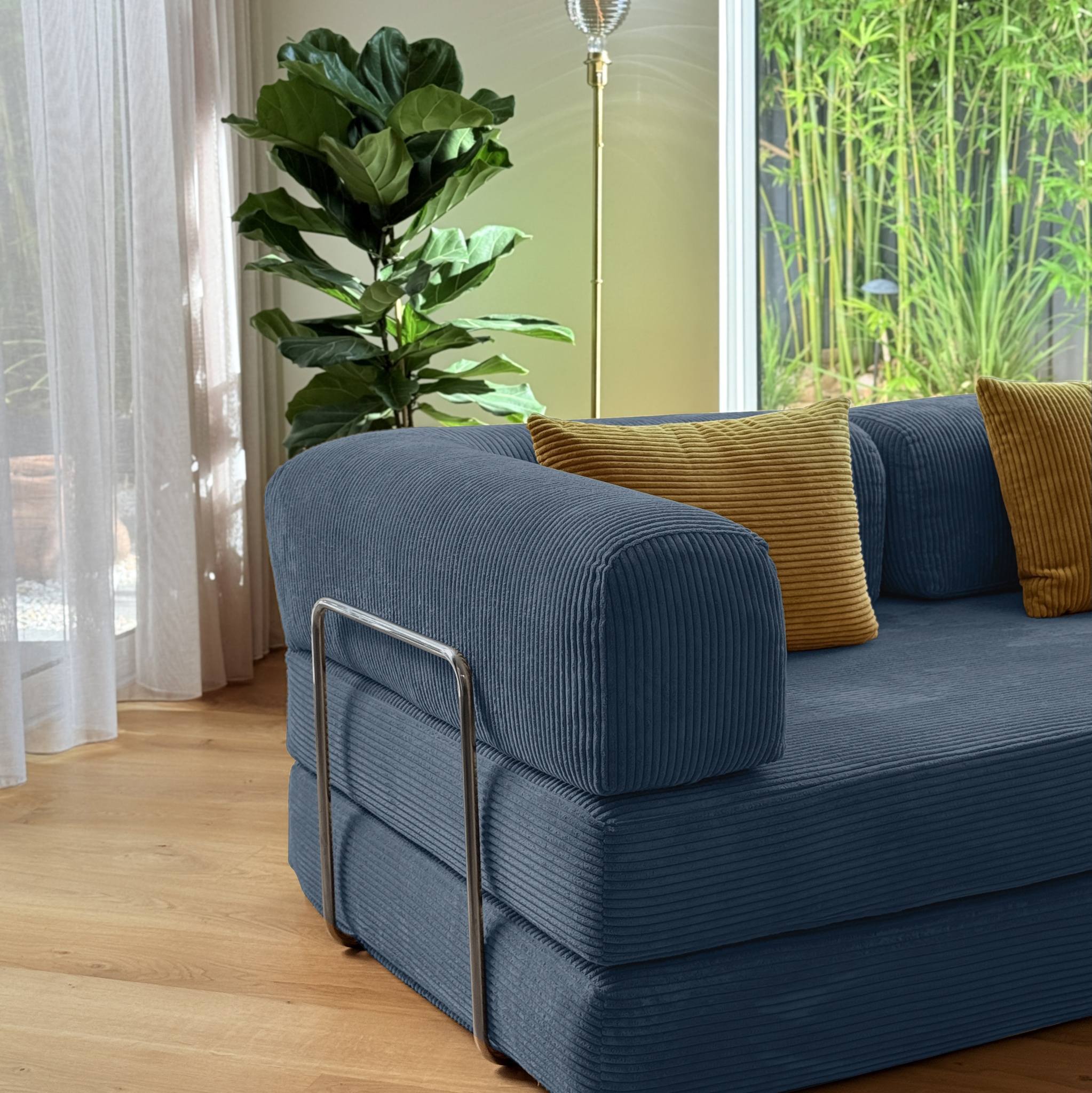 Blue sofa with yellow cushions in a room with plants and curtains