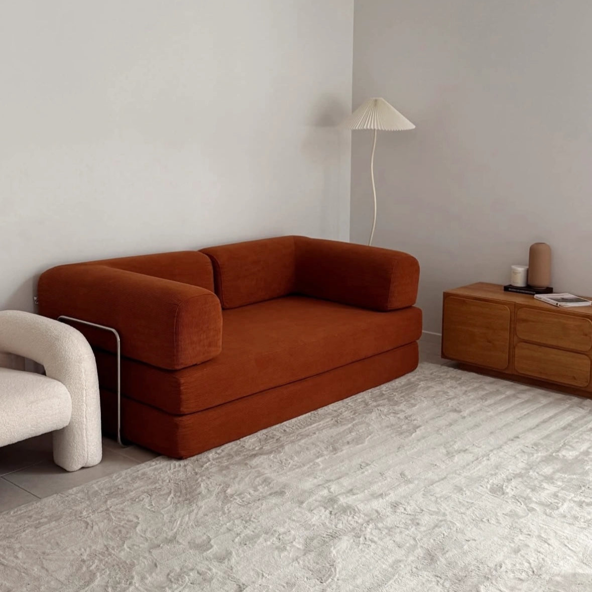 Modern living room with a brown sofa, white armchair, and wooden side table.