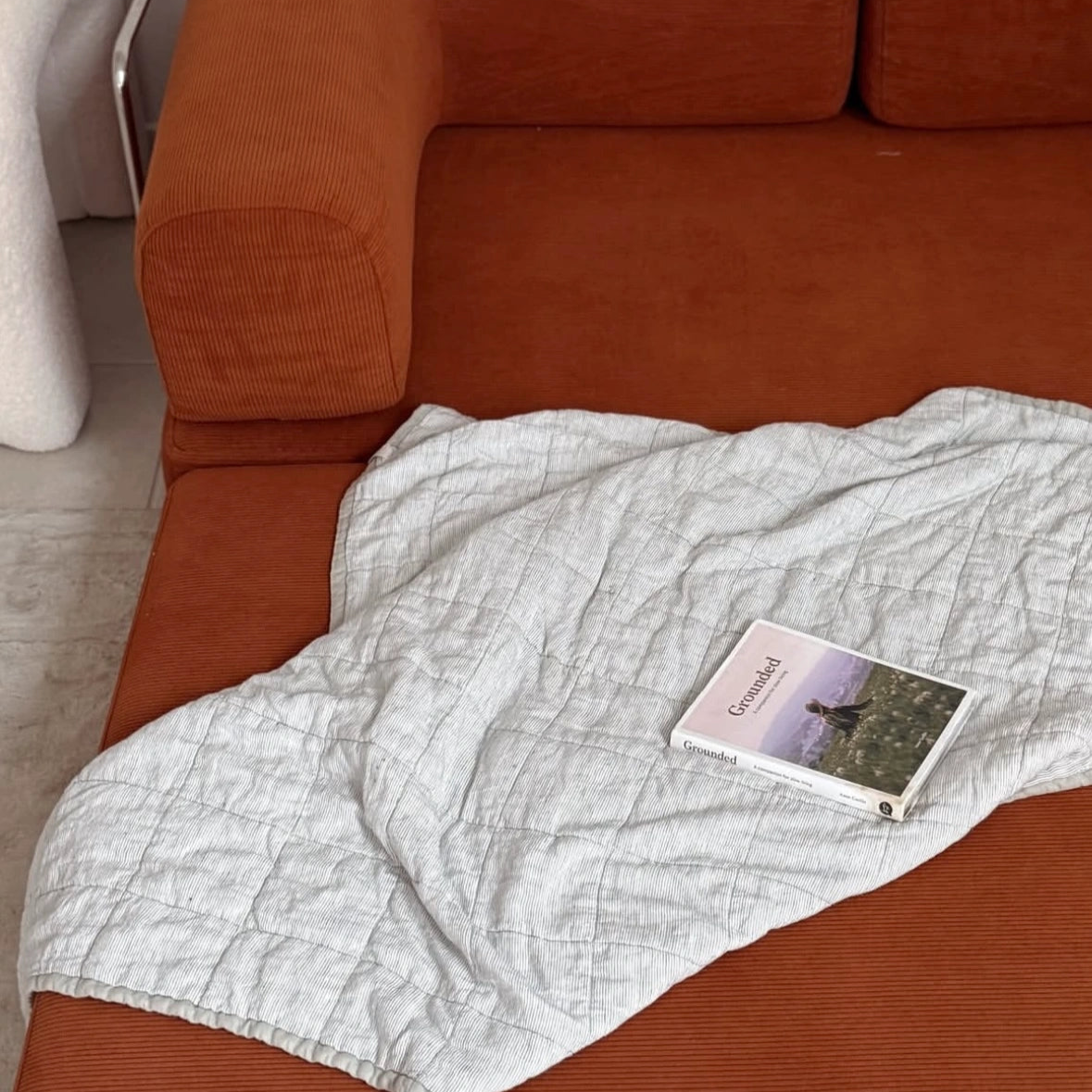 Orange sofa with a white blanket and a book on top, in a room setting.