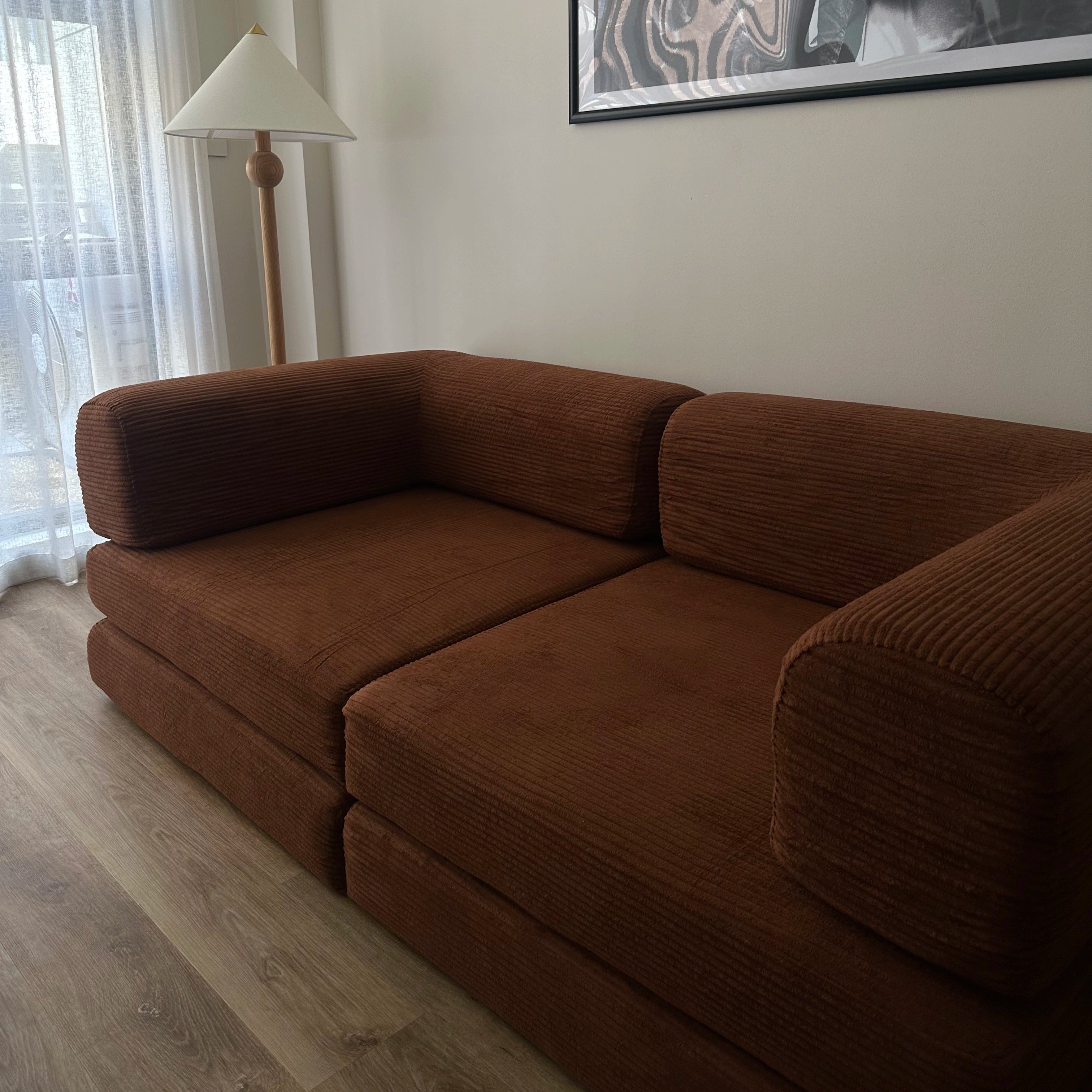 Brown sofa in a room with a lamp and artwork on the wall.