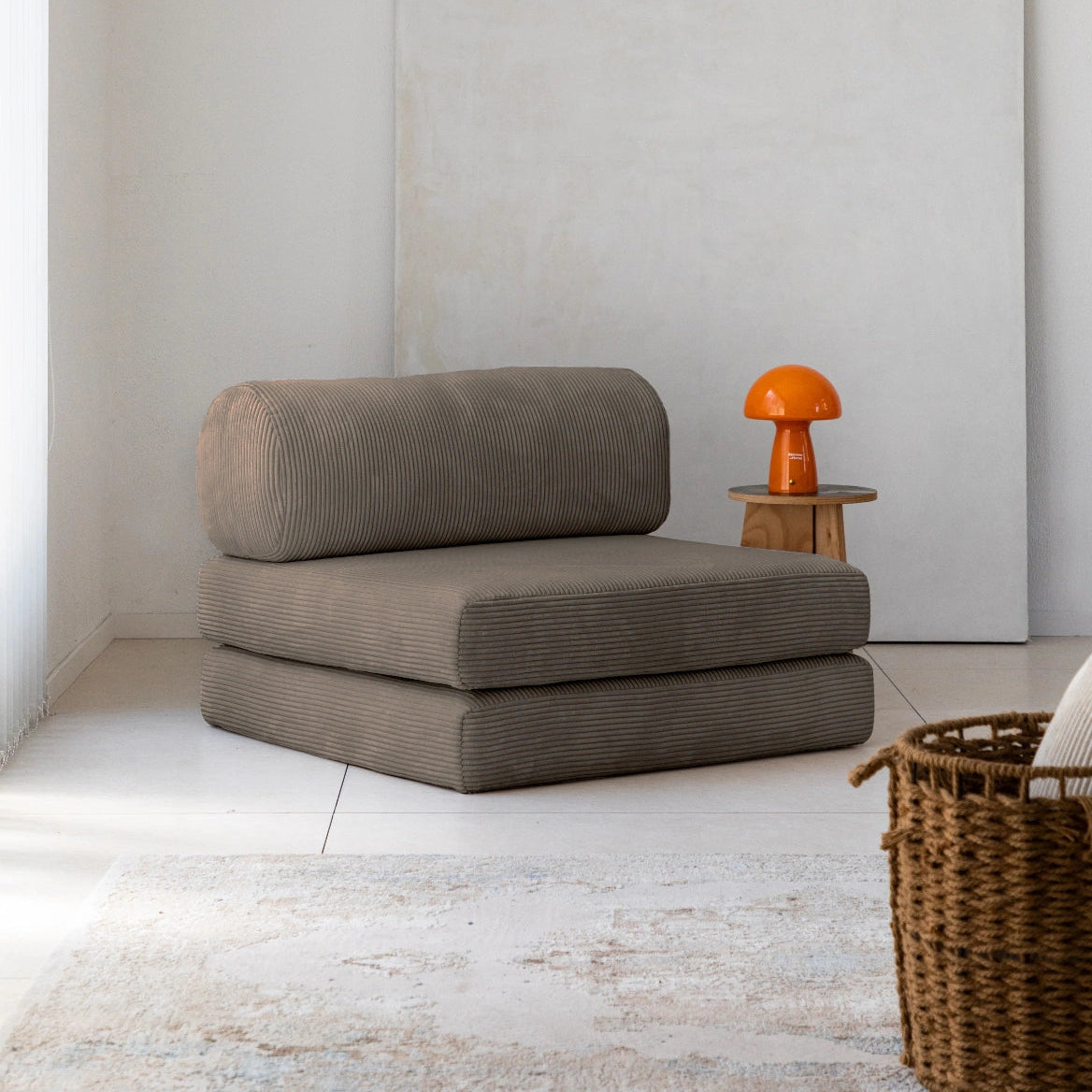 Coffee cushioned chair in a minimalistic room with a white wall and wooden floor.