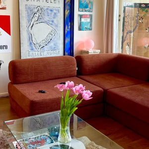Living room with a chestnut sectional sofa, glass coffee table, and pink tulips.