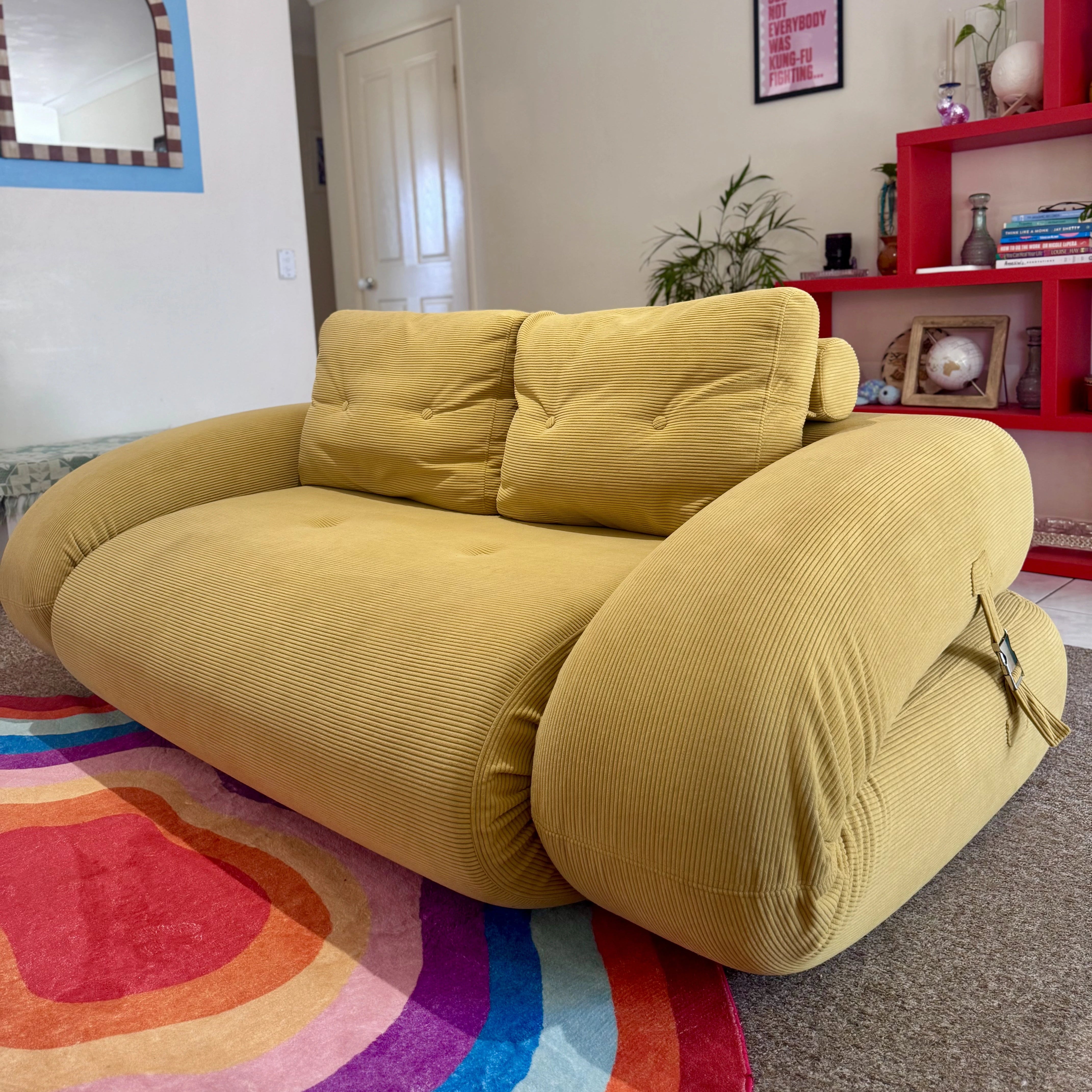 Yellow sofa in a living room with a colorful rug and decorative items on shelves.