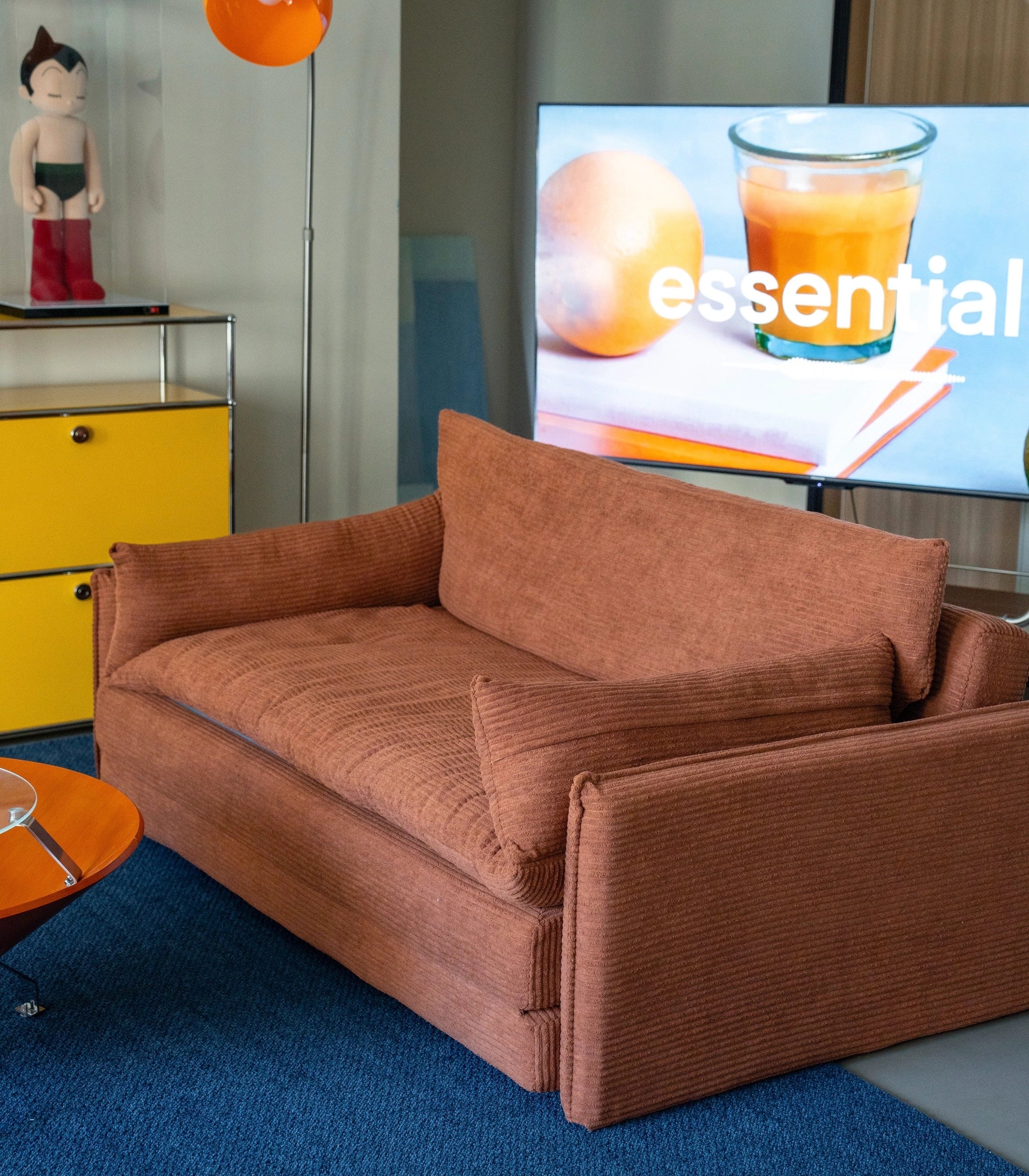 Brown sofa in a living room with a TV displaying an orange juice advertisement.