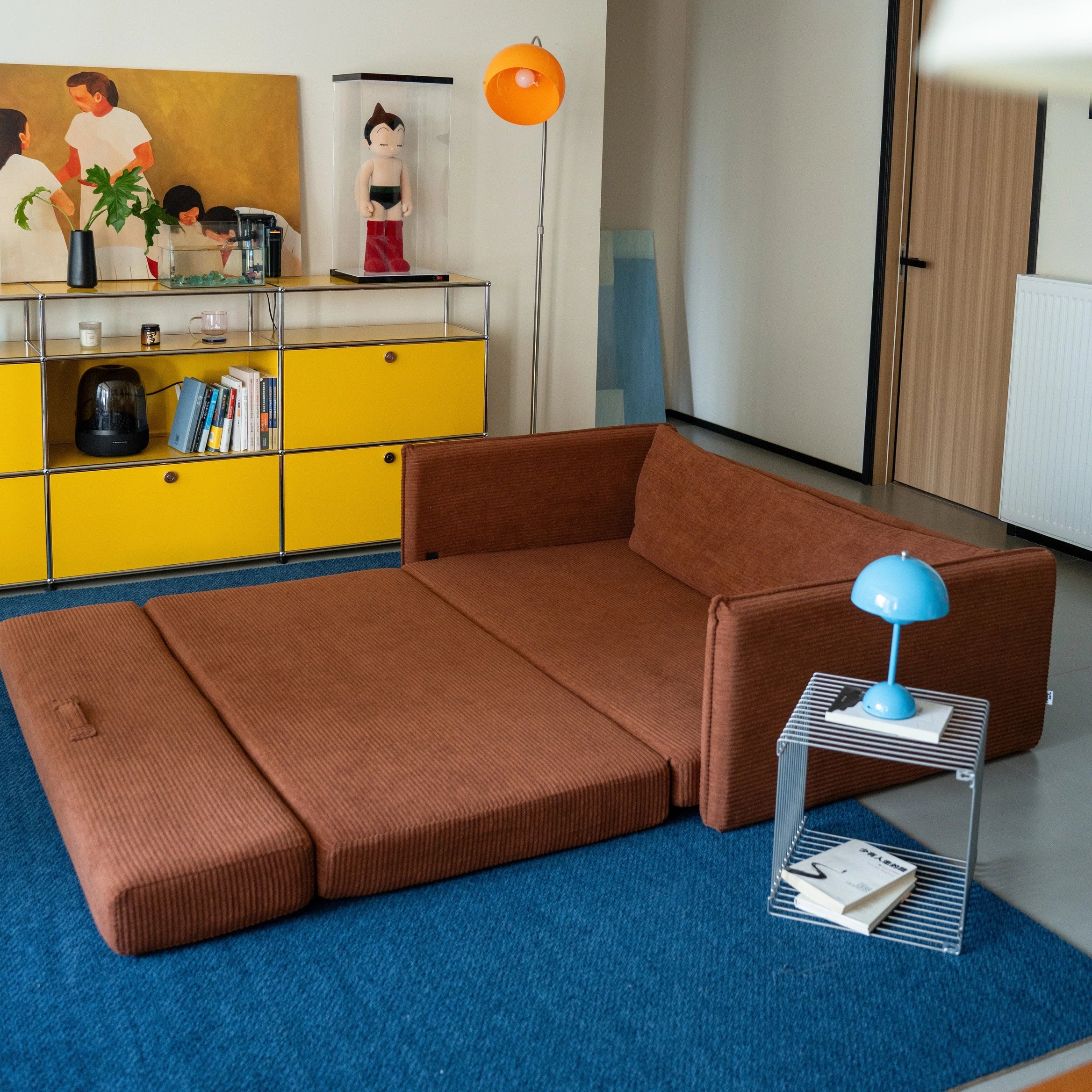 Living room with brown sectional sofa, yellow cabinet, and blue rug.