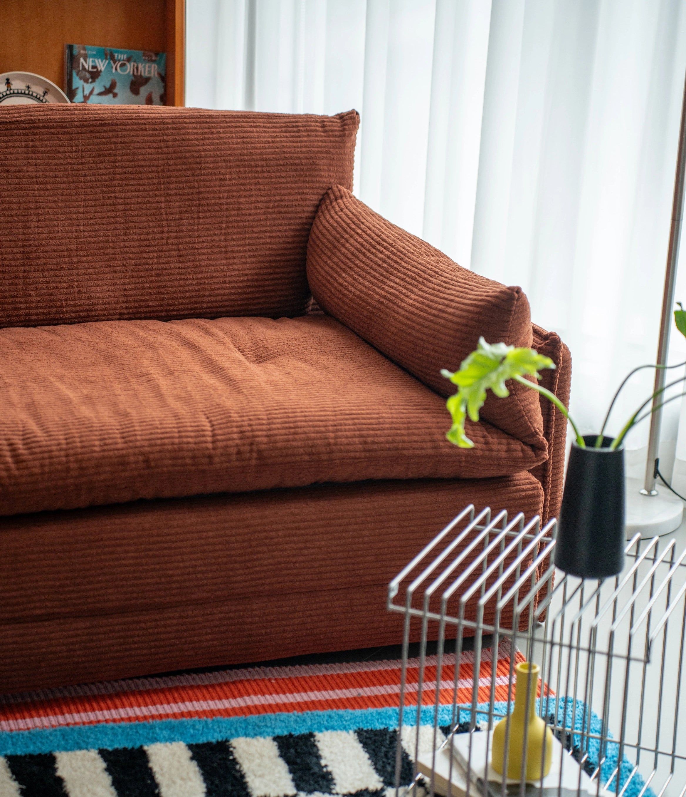 Brown sofa in a living room with a birdcage and colorful rug.