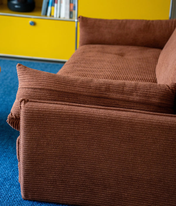 Brown corduroy sofa against a yellow wall with books on a shelf.