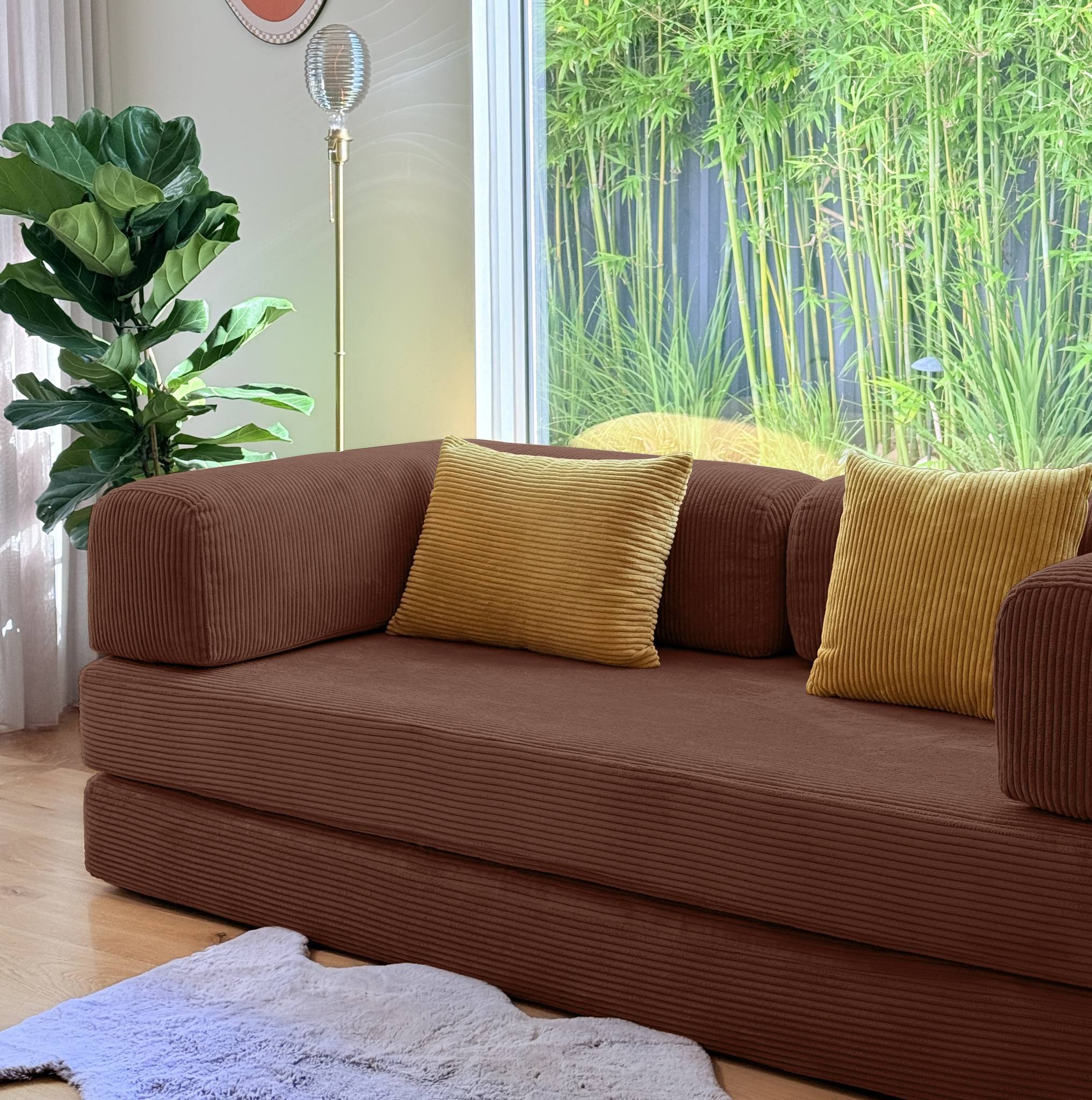 Brown sofa with yellow cushions in a room with a large window and greenery.
