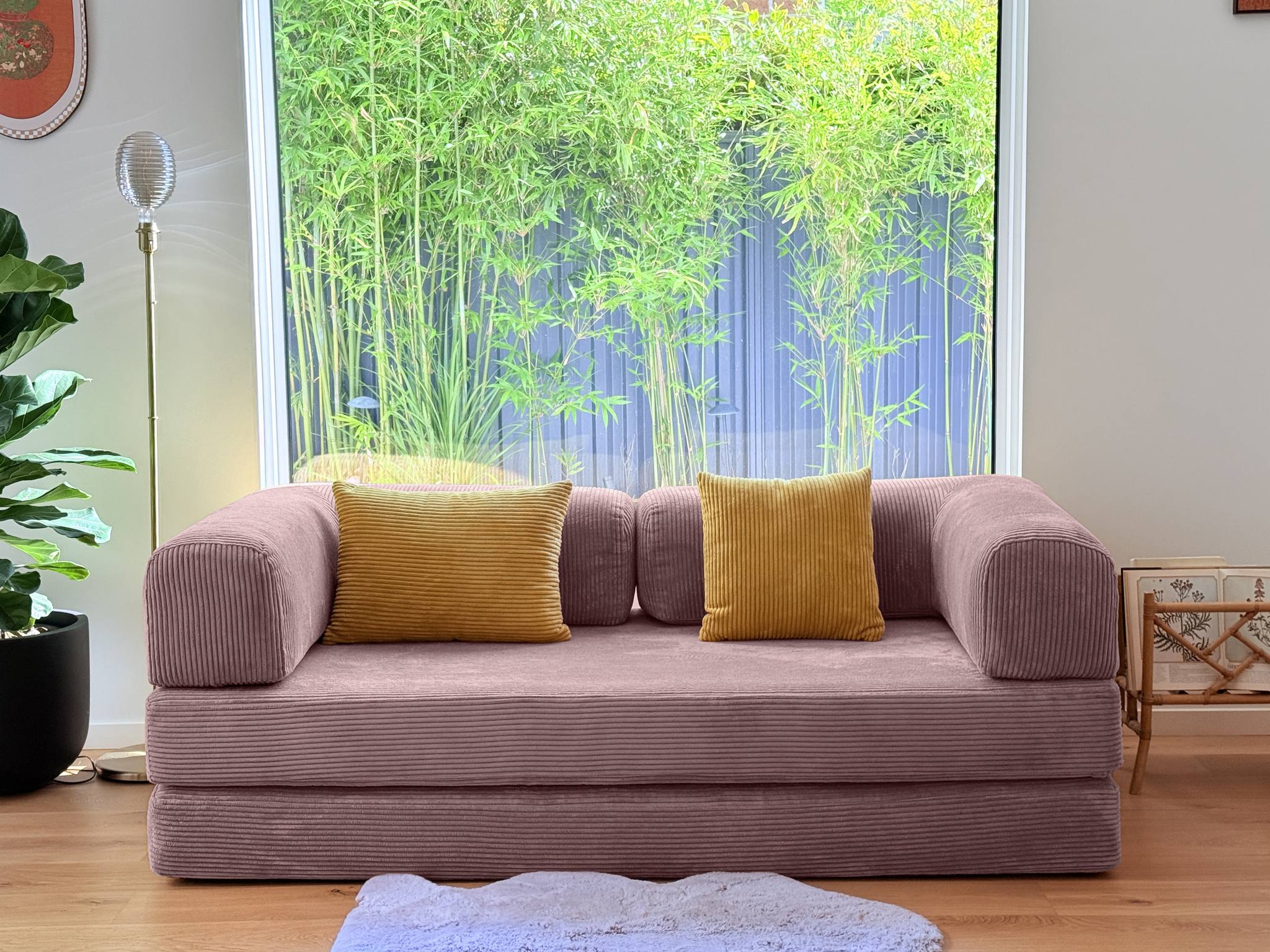 Pink sofa with yellow cushions in a room with large windows and greenery outside