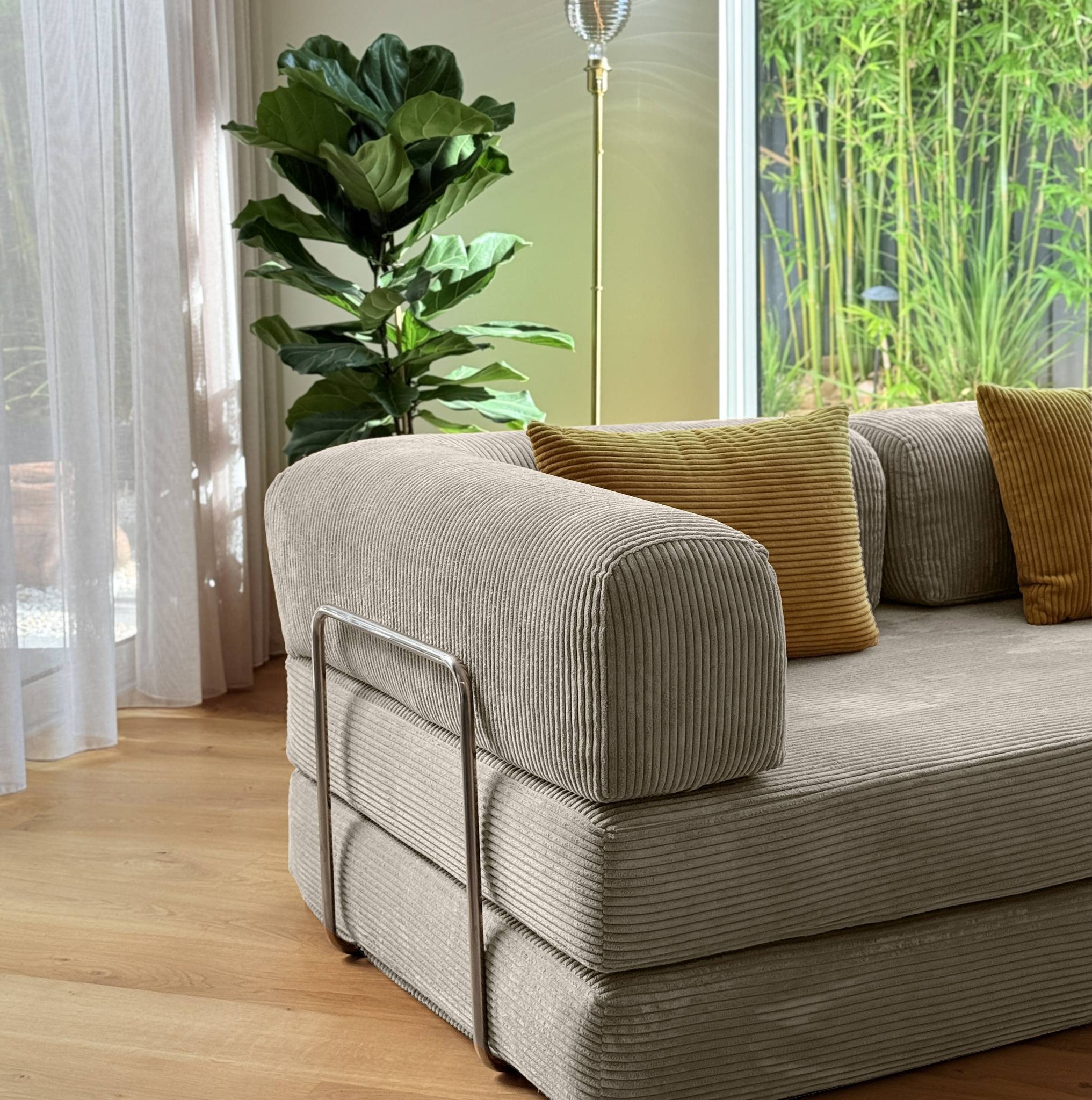 Beige sofa with brown cushions in a room with plants and a window.