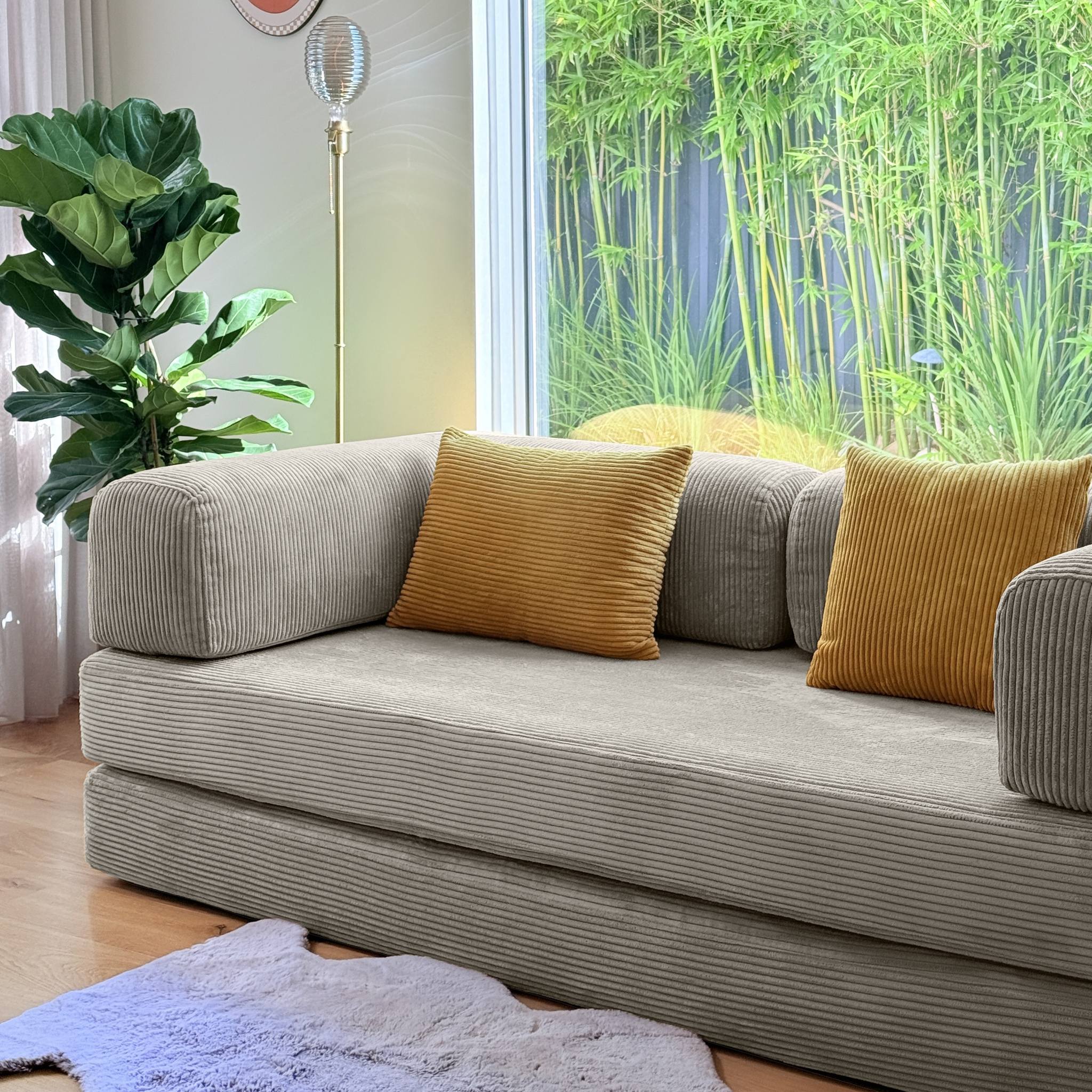 eggshell sofa with yellow cushions in a room with a large window and greenery.