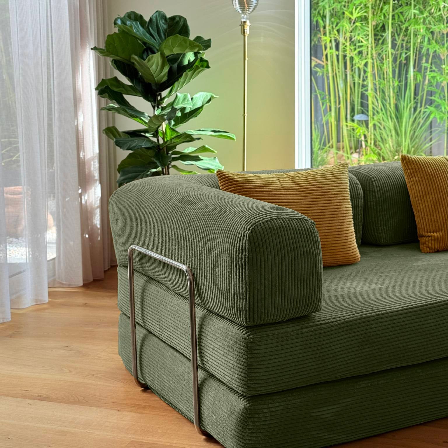Green sofa with orange cushions in a room with a large window and plant