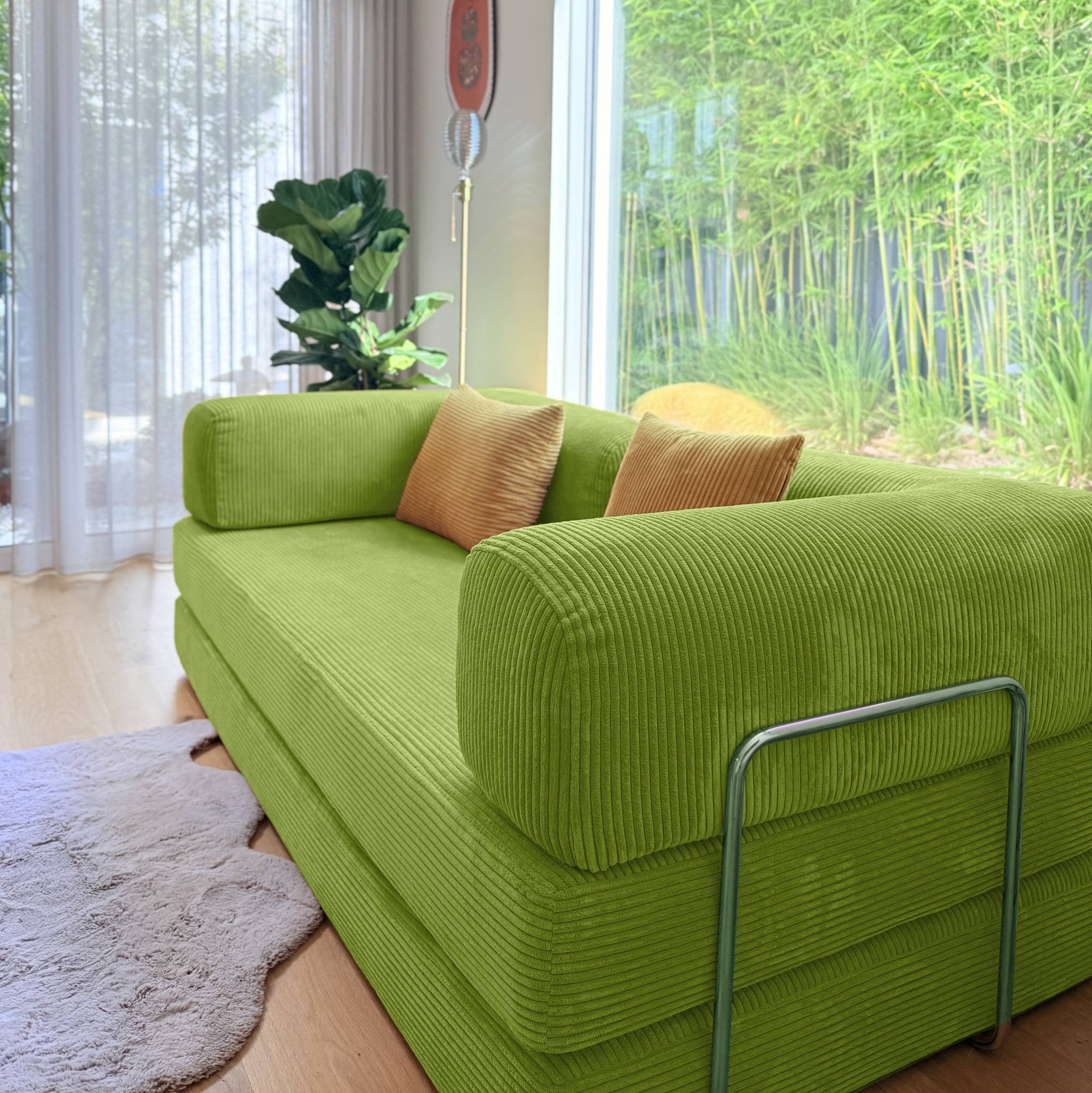 Green sofa with brown cushions in a room with large windows and plants.