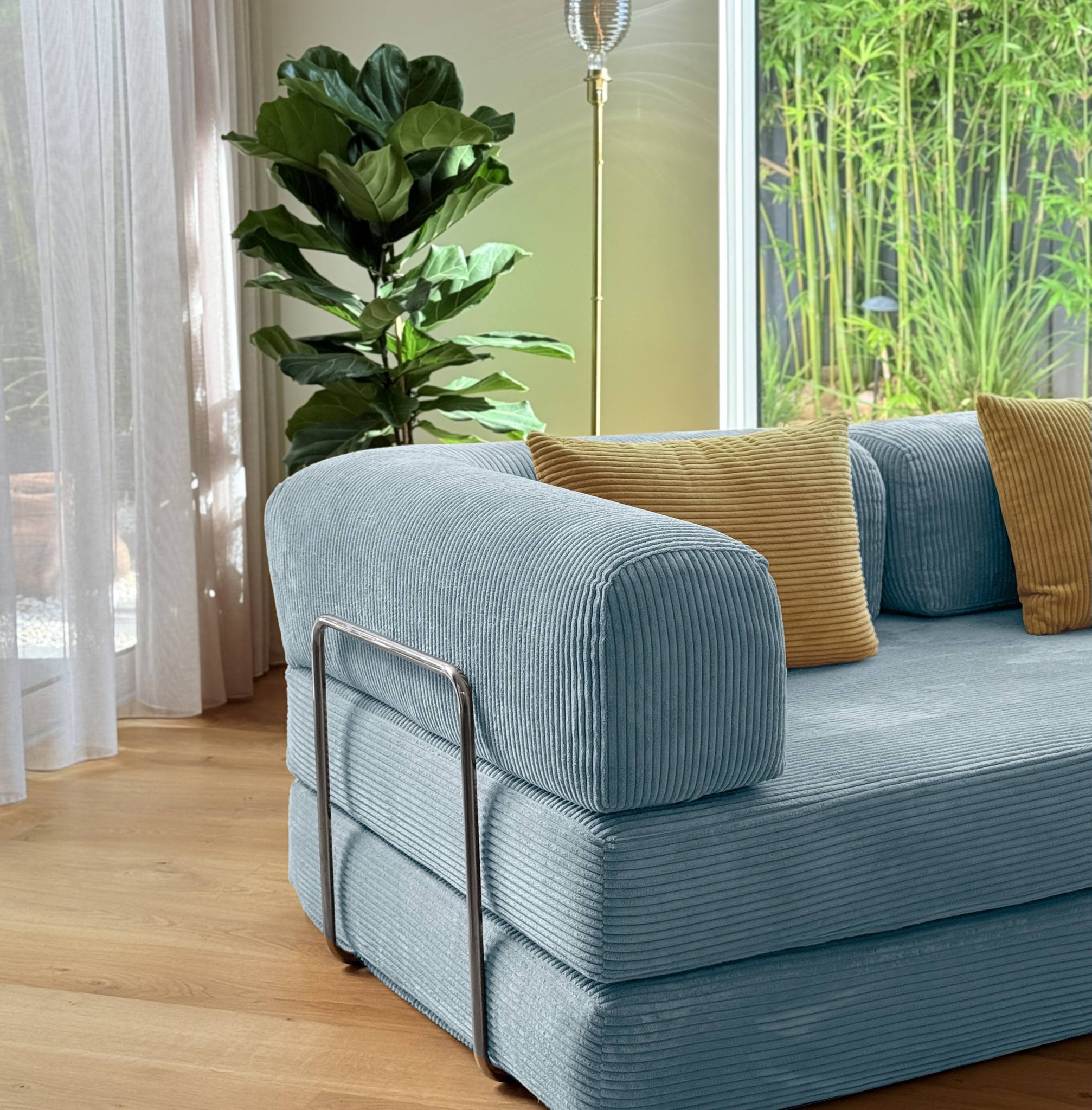 Blue sofa with gold pillows in a room with plants and a lamp.