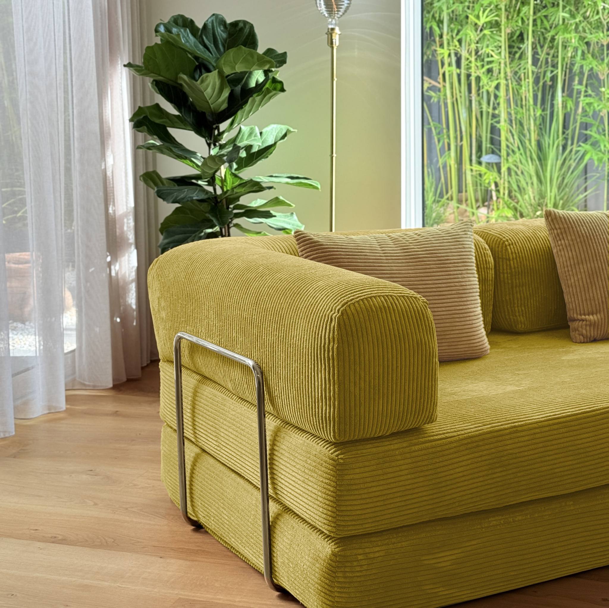 Yellow sofa with brown cushions in a room with a plant and window.
