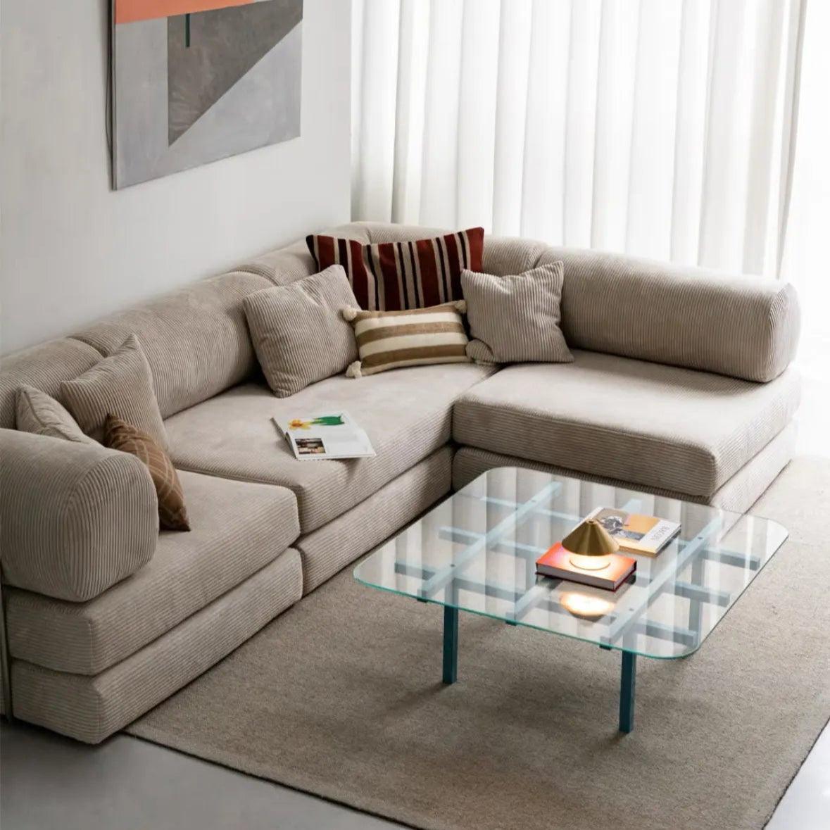 Beige sectional sofa with decorative pillows and a glass coffee table in a living room.